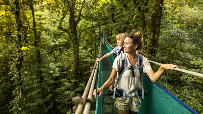 A woman and child walk across a hanging bridge in rainforest canopy