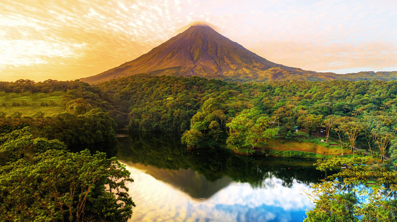 Arenal Volcano rises over a forest and reflective lake