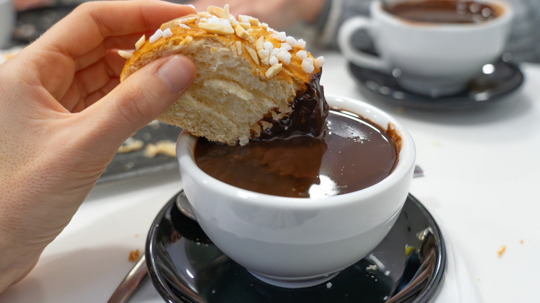 Spanish pastries being dipped in a creamy hot chocolate