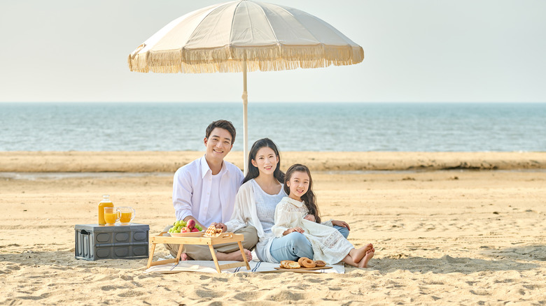 A family poses under a fringed parasol on the beach in South Korea