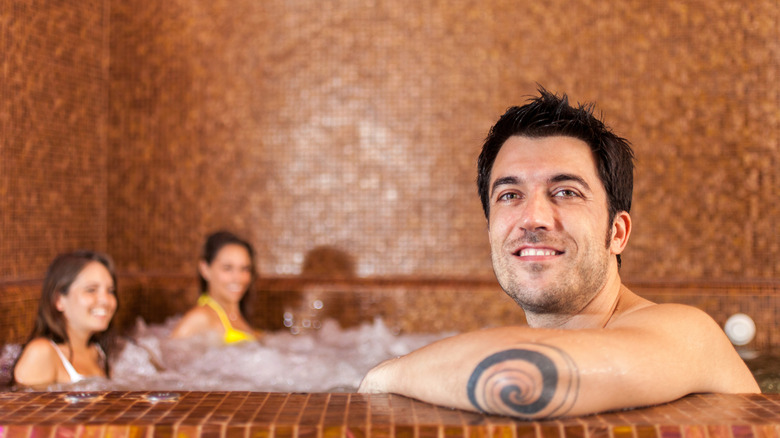 A man with a tattoo soaking in a spa with two women in the background