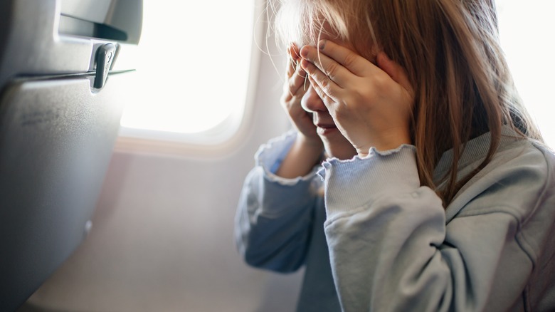 Child on plane covering eyes