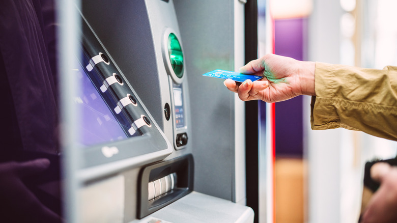 A woman holds a card in front of an ATM