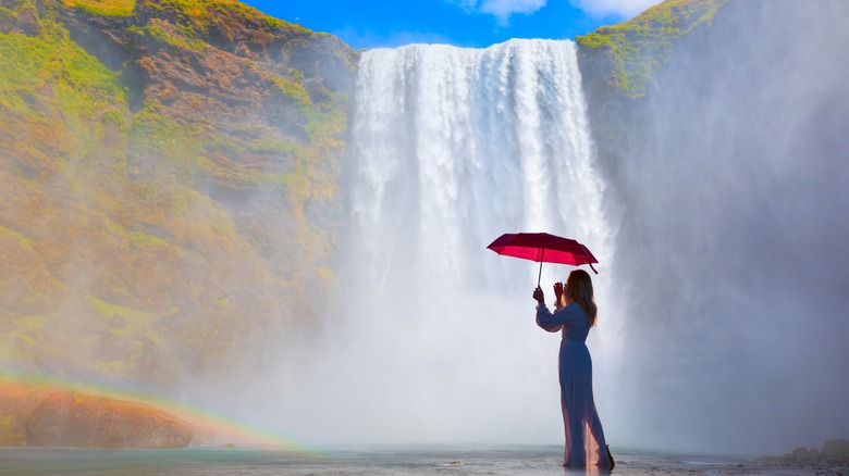 person holding umbrella beside waterfall