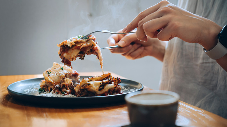 Closeup of hands cutting lasagna