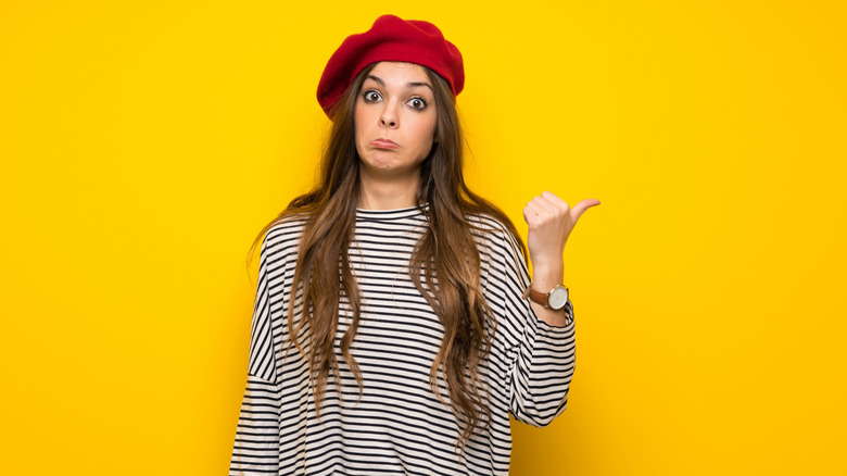 A woman in a beret frowns and sticks our her thumb