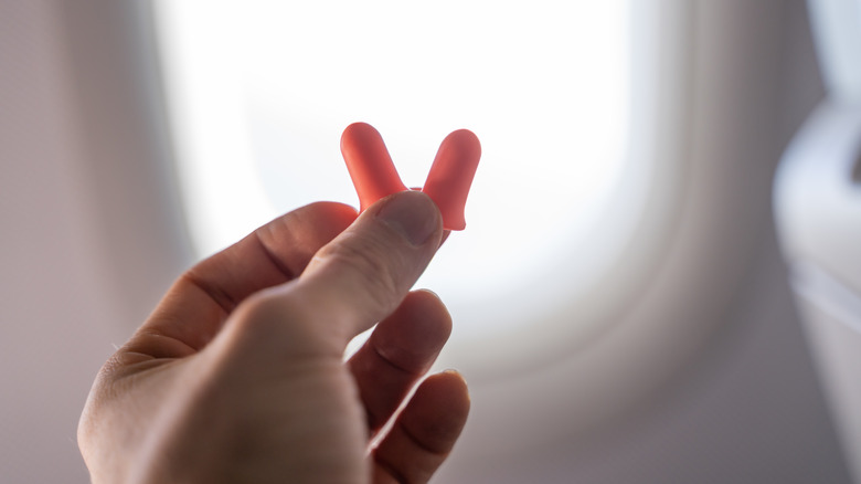 Hand holding two earplugs in airplane