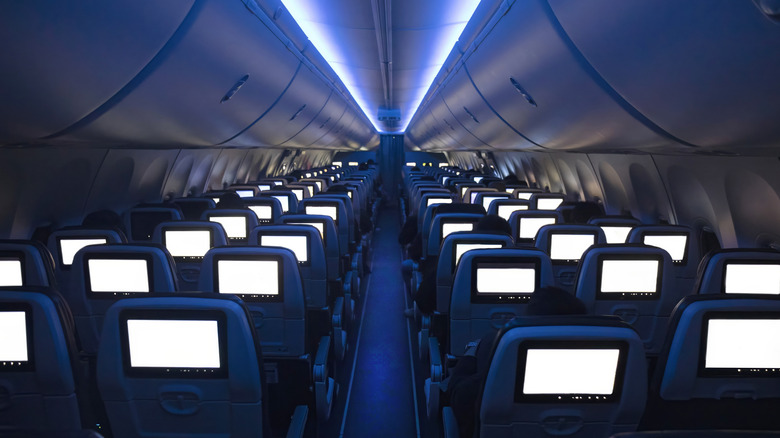 Inside a flight cabin, with lights dimmed and empty seats.