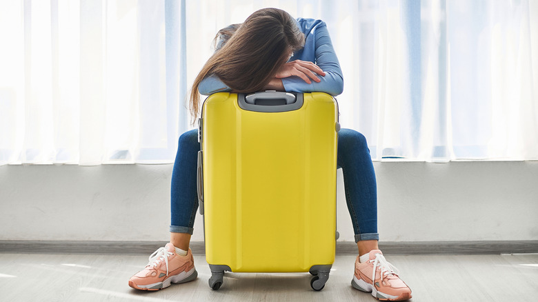 A woman sits with her head down and arms crossed on a yellow suitcase.