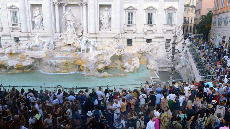 A large crowd gathers around a temporary barrier at the Trevi Fountain