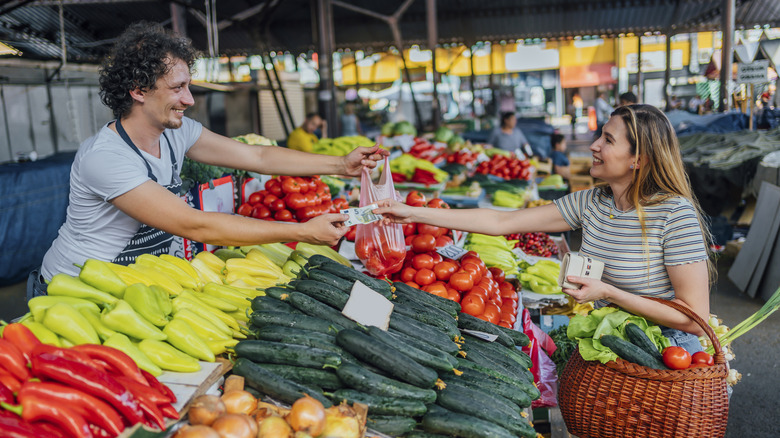 A woman buys tomatoes from a vendor at a European market