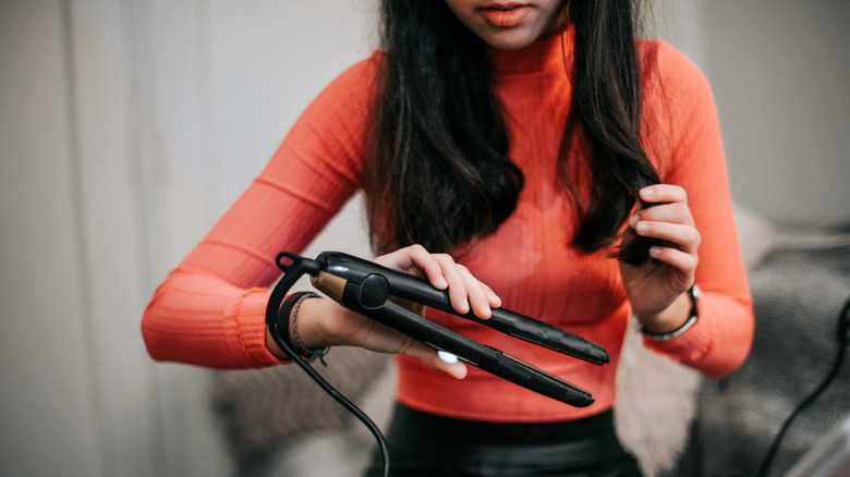 Long-haired woman using hair straightener