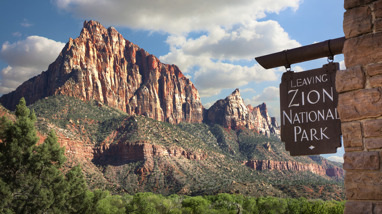 Sign leaving Zion National Park with sandstone cliffs in the background